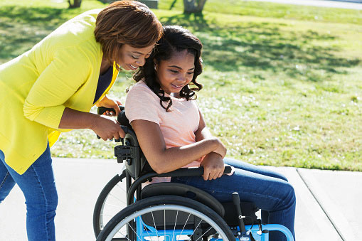 batang babae sa isang wheelchair na may katulong