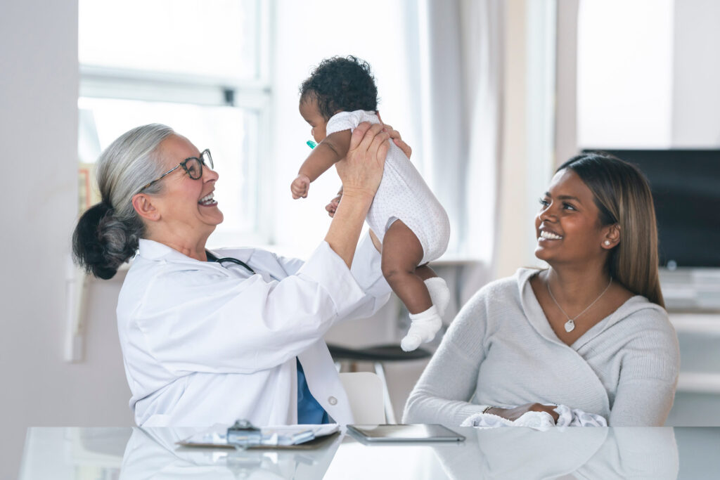 Baby being held by a doctor for a check-up with the mother watching and smiling