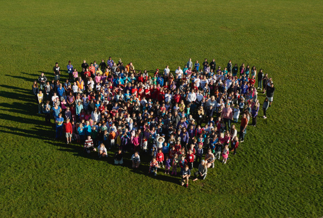 A large group of people arranged in a heart shape on a grassy field