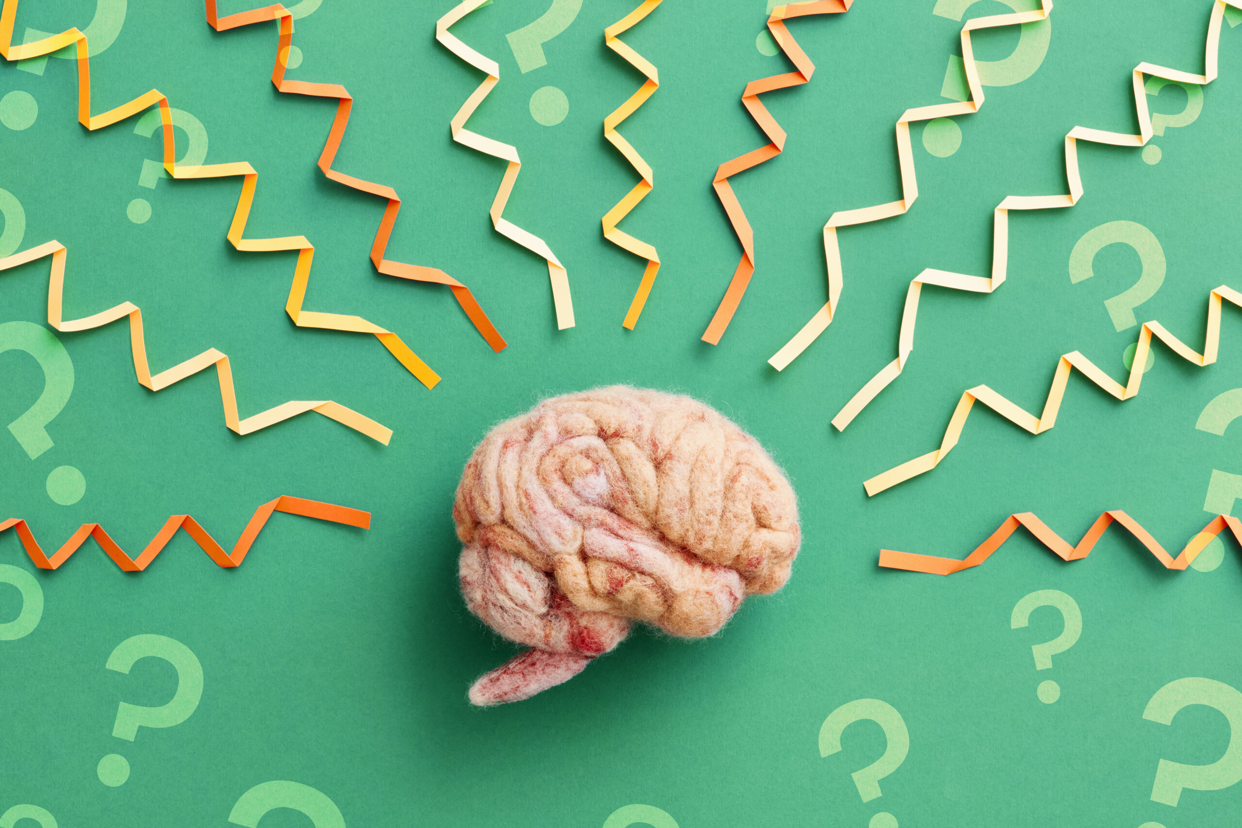 A human brain model with folded paper brainwaves and question marks