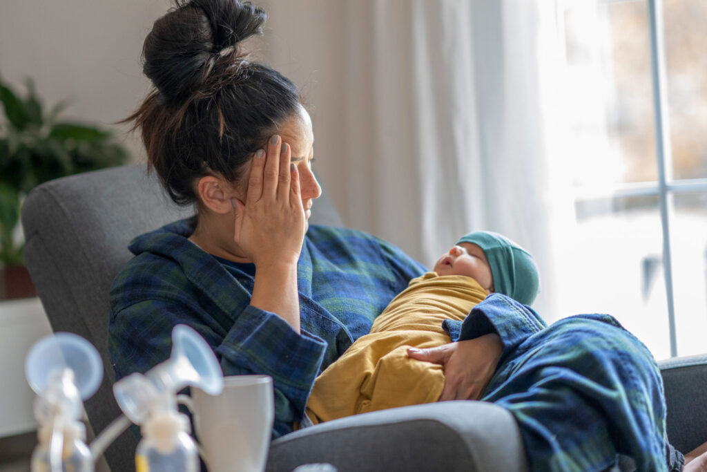 Mother holding newborn at home with hand on her head as a tired expression