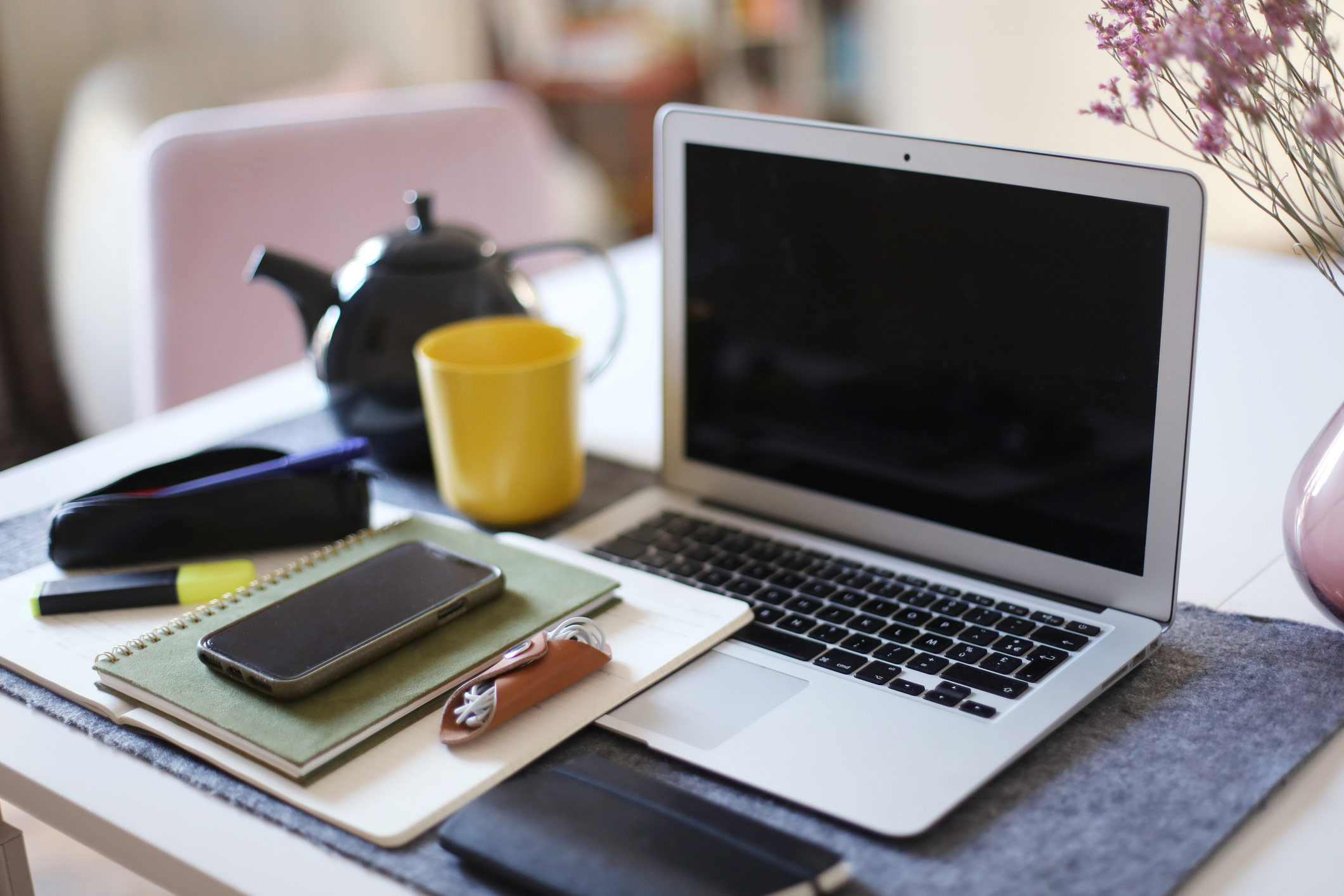 A quaint work from home setup with a laptop, notebook, cell phone, and earphones.